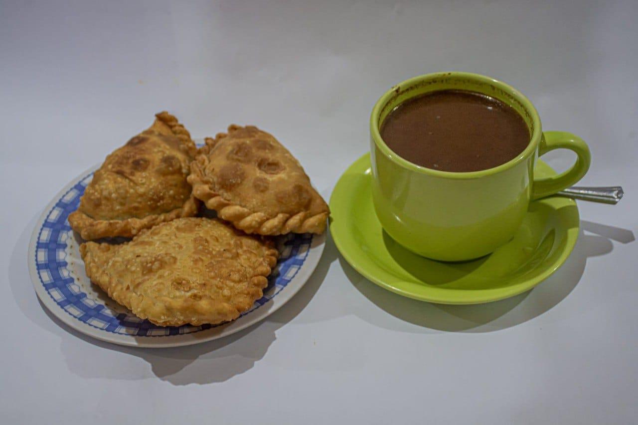 EMPANADAS CON CHOCOLATE: LAS EMPANADAS SON MASAS  ELABORADA A BASE DE HARINA DE TRIGO Y QUESO RAYADO, LUEGO FRITAS QUE SE ACOMPAÑA CON UNA TAZA DE CHOCOLATE